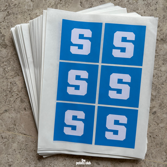 Bulk Stickers Stack of blue and white stickers with 'S' on a textured surface