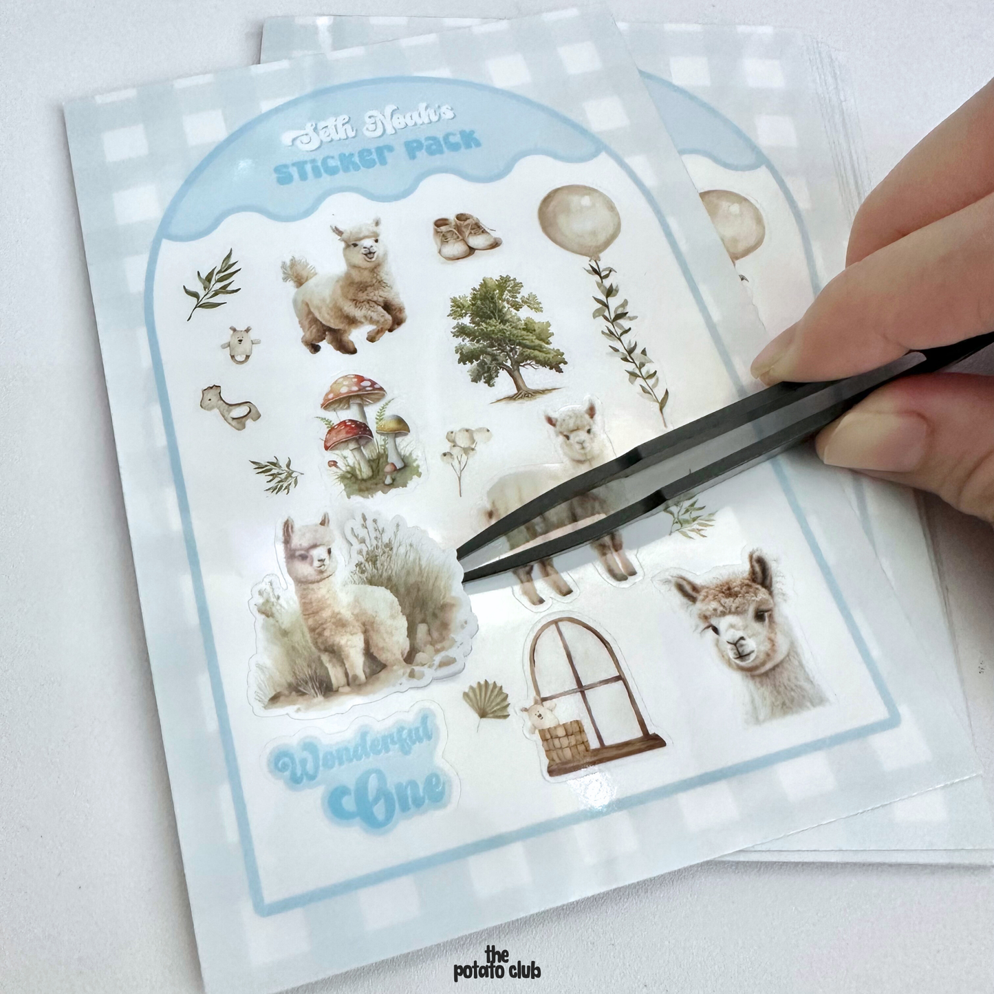 Sticker pack with alpaca designs and a hand using tweezers to pick up a sticker.