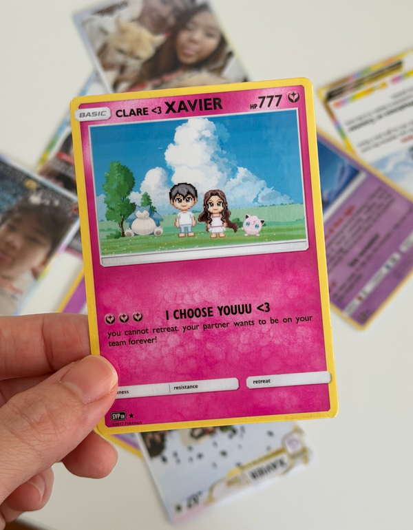 A hand holds a custom anime-style trading card featuring Clare and Xavier with a pink and yellow border. The card has a yellow border, a pink bottom half, and a colorful illustration in the center.