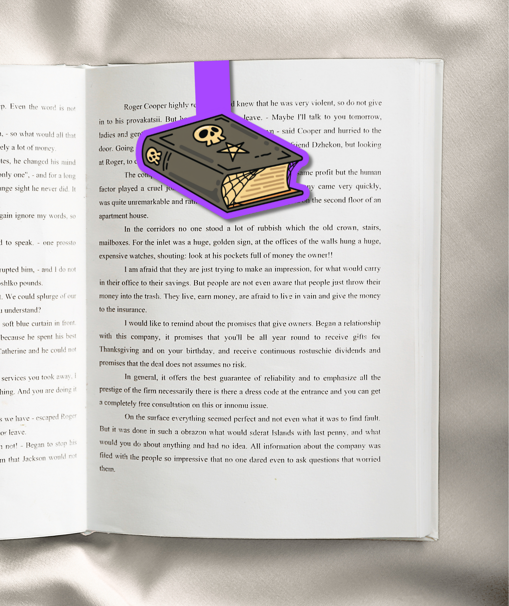 A purple and gold ribbon bookmark shaped like a stylized book with a ribbon loop, shown wrapped around an open book page.